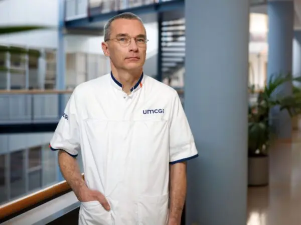 Persoon in een witte zorgjas staat in de hal van een ziekenhuisgebouw.