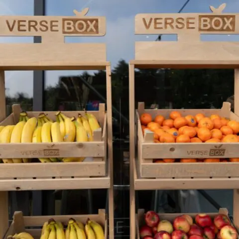Houten fruitrekken van VerseBox gevuld met bananen, mandarijnen en appels voor een glazen gevel.