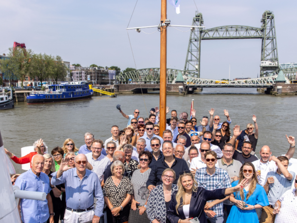 Grote groep mensen op een boot in de haven, met op de achtergrond een hefbrug en gebouwen langs het water.