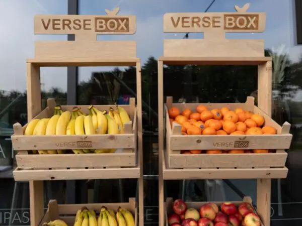 Houten fruitrekken van VerseBox gevuld met bananen, mandarijnen en appels voor een glazen gevel.